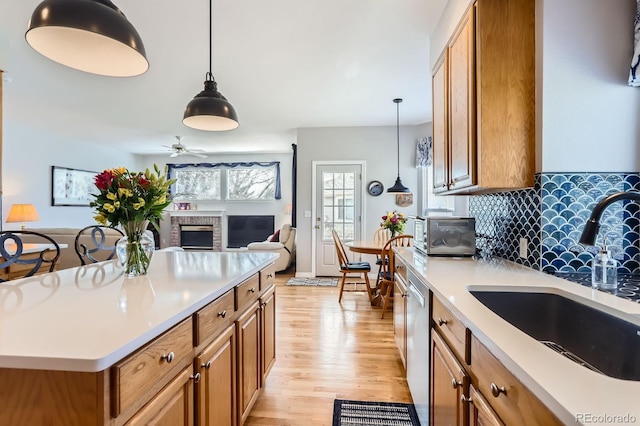 kitchen featuring dishwasher, a sink, light countertops, light wood-style floors, and brown cabinetry