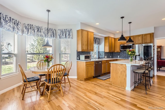 kitchen with light wood-style flooring, appliances with stainless steel finishes, light countertops, and a healthy amount of sunlight