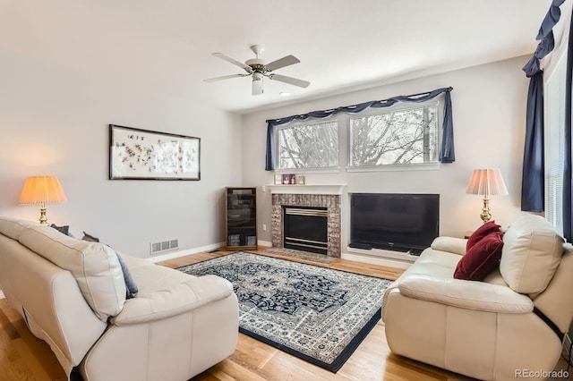 living area with visible vents, baseboards, a brick fireplace, a ceiling fan, and wood finished floors
