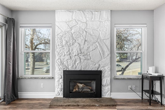 interior details with a textured ceiling, a stone fireplace, baseboards, and wood finished floors