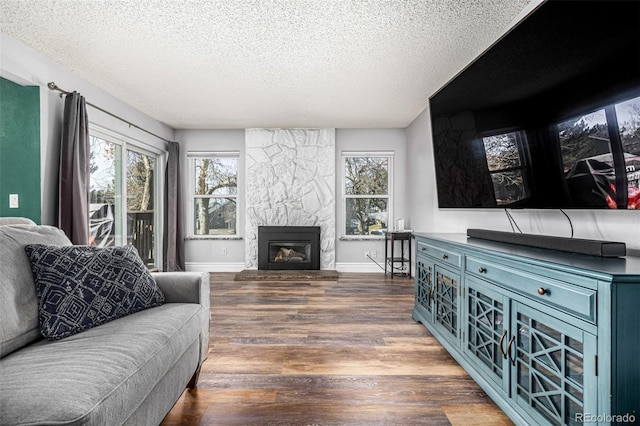 living room featuring a textured ceiling, a fireplace, wood finished floors, and a healthy amount of sunlight