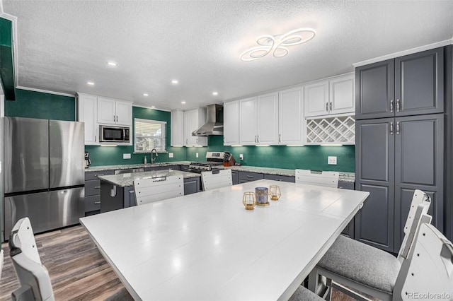 kitchen featuring a kitchen island, white cabinetry, light countertops, appliances with stainless steel finishes, and wall chimney range hood