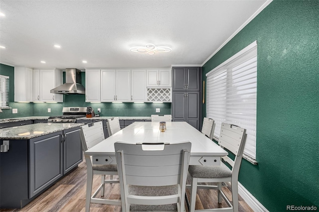 kitchen with wood finished floors, white cabinets, wall chimney range hood, a center island, and gas range