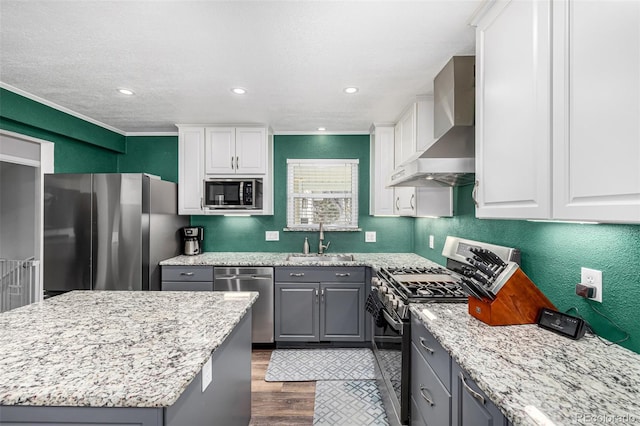 kitchen featuring white cabinets, gray cabinets, stainless steel appliances, wall chimney range hood, and a sink