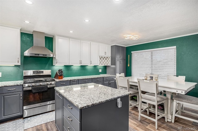 kitchen with gray cabinetry, wood finished floors, white cabinetry, wall chimney range hood, and stainless steel gas stove