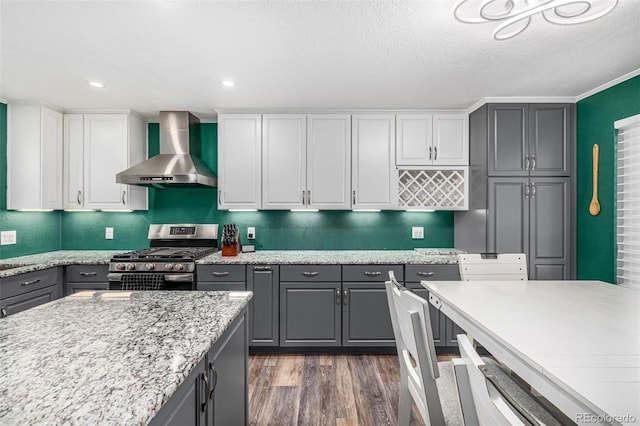 kitchen featuring dark wood-style floors, gray cabinetry, wall chimney range hood, and stainless steel gas range oven