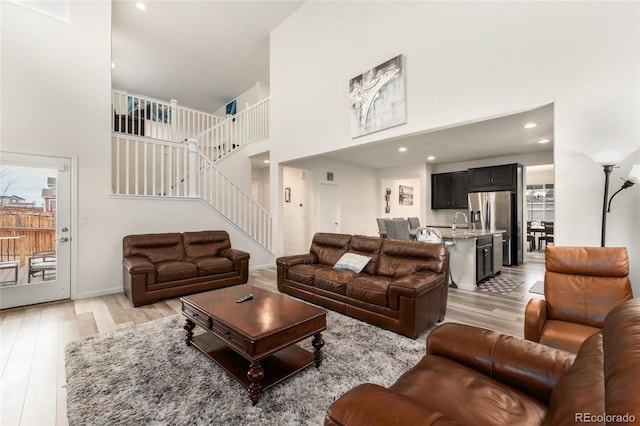 living room featuring a high ceiling, sink, and light hardwood / wood-style flooring