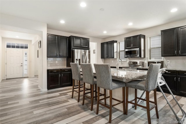 kitchen with a kitchen bar, light stone counters, light hardwood / wood-style flooring, an island with sink, and stainless steel appliances