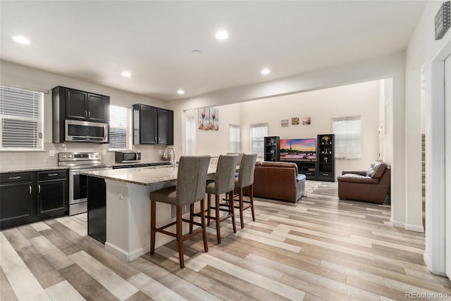 kitchen featuring a breakfast bar area, tasteful backsplash, a center island with sink, stainless steel appliances, and light stone countertops