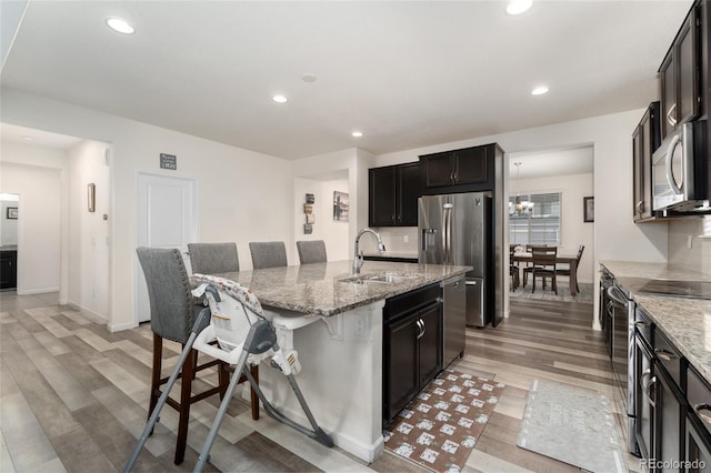 kitchen featuring sink, a kitchen bar, a kitchen island with sink, light stone counters, and stainless steel appliances