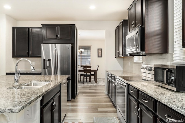 kitchen featuring sink, decorative backsplash, stainless steel appliances, light stone countertops, and light hardwood / wood-style flooring