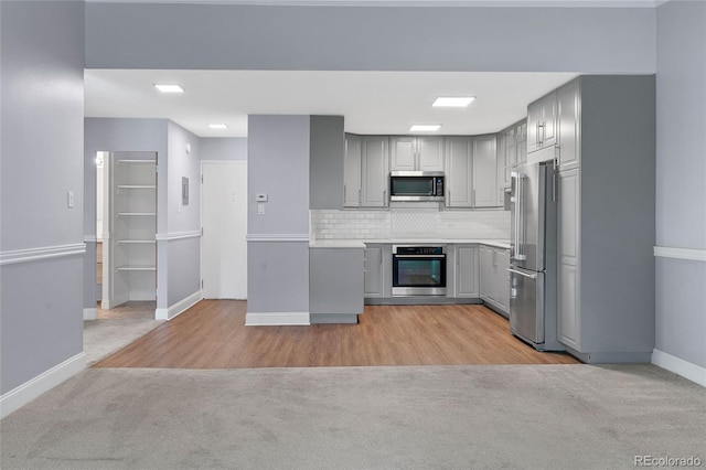 kitchen featuring gray cabinetry, light hardwood / wood-style floors, decorative backsplash, and stainless steel appliances