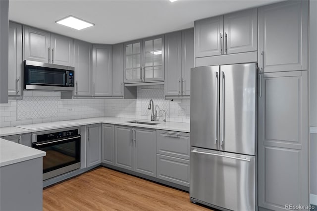 kitchen with stainless steel appliances, light hardwood / wood-style flooring, tasteful backsplash, sink, and gray cabinets