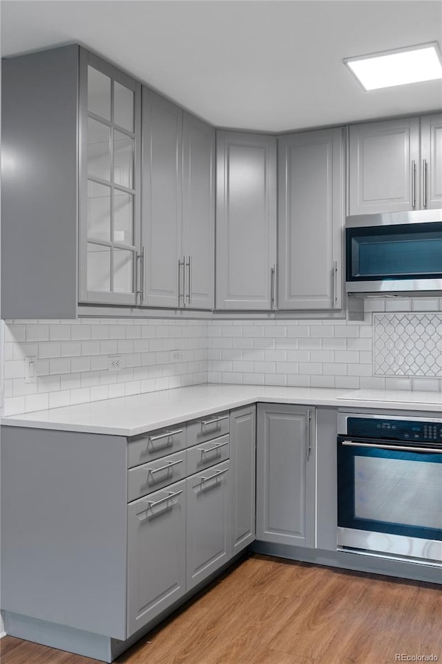 kitchen featuring light wood-type flooring, appliances with stainless steel finishes, backsplash, and gray cabinetry