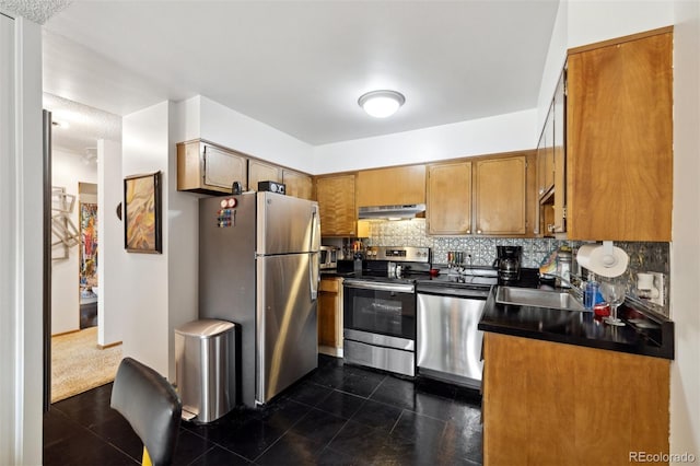 kitchen with dark countertops, decorative backsplash, appliances with stainless steel finishes, a sink, and under cabinet range hood