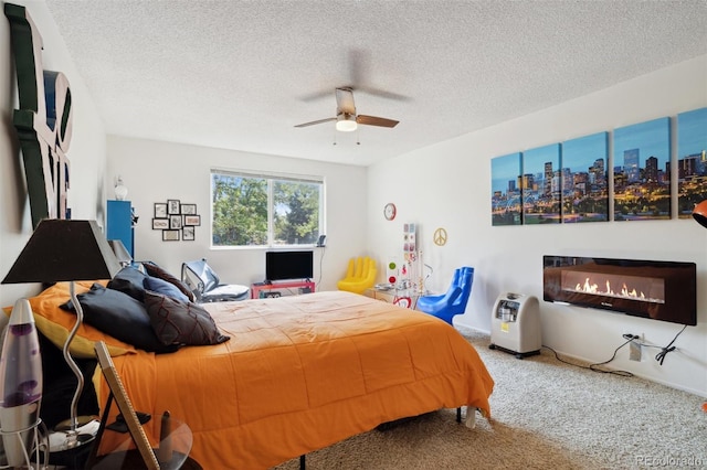 carpeted bedroom featuring a ceiling fan, a textured ceiling, and a glass covered fireplace