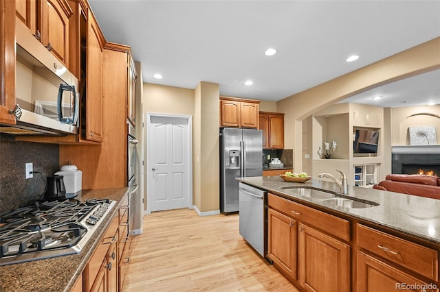 18967 W 54th Ln, Golden, CO 80403 - kitchen with a sink, appliances with stainless steel finishes, dark stone countertops, decorative backsplash, and light wood finished floors