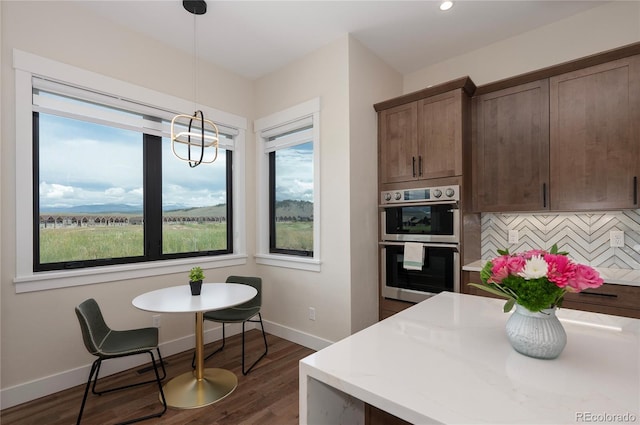 kitchen with hanging light fixtures, decorative backsplash, a wealth of natural light, dark hardwood / wood-style flooring, and stainless steel double oven