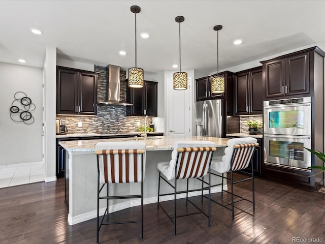 5445 Verbena St, Denver, CO 80238 - kitchen with wall chimney range hood, stainless steel appliances, backsplash, dark wood-style flooring, and a breakfast bar area