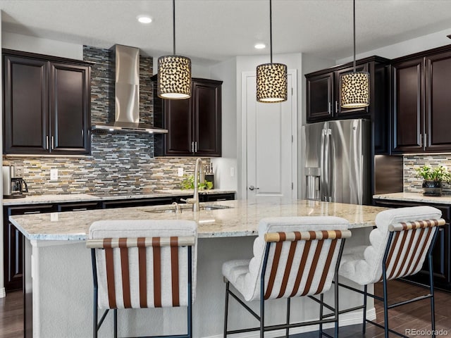 5445 Verbena St, Denver, CO 80238 - kitchen featuring wall chimney exhaust hood, stainless steel refrigerator with ice dispenser, a center island with sink, tasteful backsplash, and light stone counters