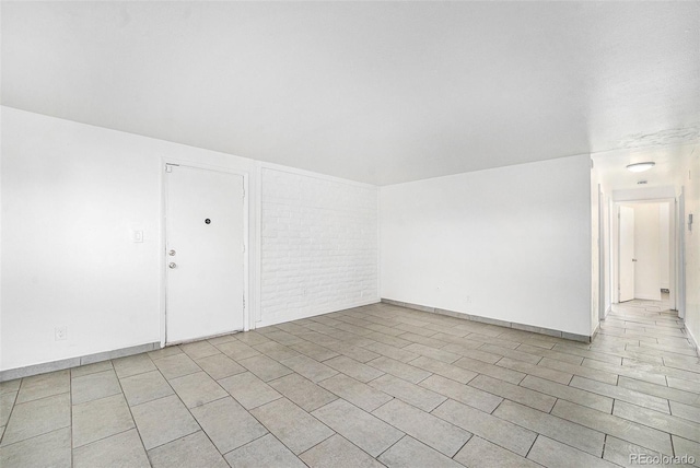 unfurnished room featuring brick wall