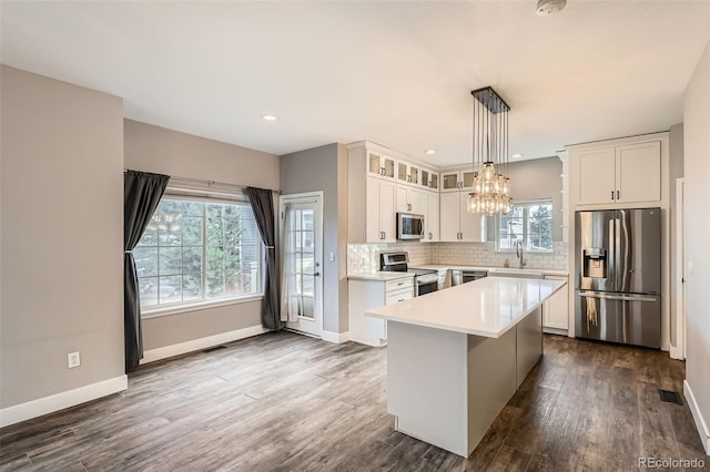 kitchen featuring white cabinets, appliances with stainless steel finishes, a center island, decorative light fixtures, and sink