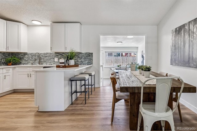 1418 5th St, Fort Lupton, CO 80621 - kitchen featuring a breakfast bar area, white cabinetry, tasteful backsplash, light countertops, and light wood-style flooring