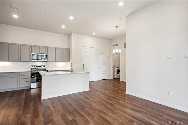 kitchen featuring decorative light fixtures, an island with sink, washer / dryer, sink, and stainless steel appliances