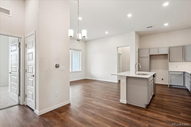 kitchen featuring an island with sink, sink, gray cabinetry, hanging light fixtures, and dark wood-type flooring