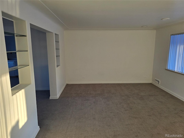 empty room with built in shelves and dark colored carpet