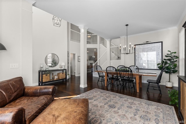 living area with stairway, dark wood-type flooring, an inviting chandelier, and ornate columns