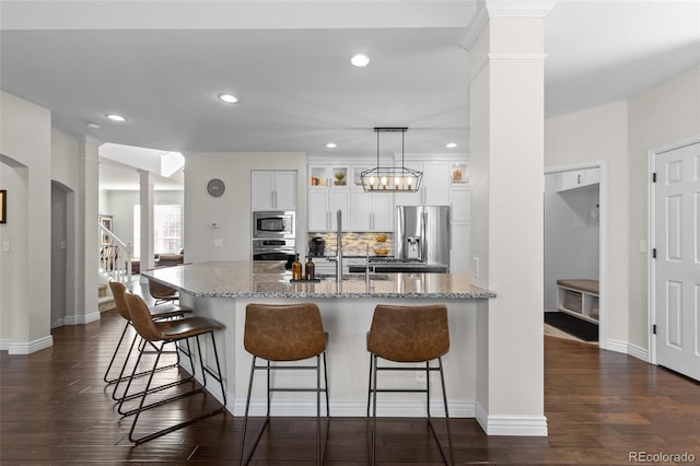 kitchen featuring a breakfast bar area, dark wood finished floors, decorative columns, appliances with stainless steel finishes, and tasteful backsplash