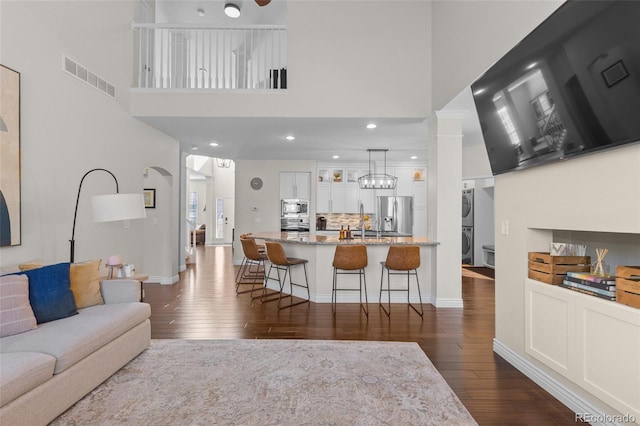 living area featuring visible vents, stacked washing maching and dryer, baseboards, and dark wood-style flooring