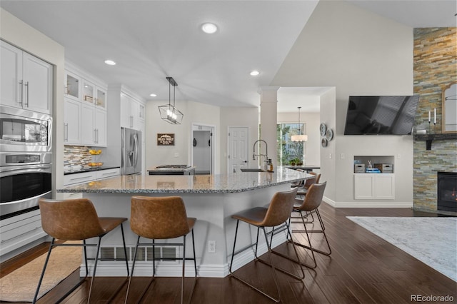 kitchen with a sink, white cabinetry, stainless steel appliances, glass insert cabinets, and light stone countertops