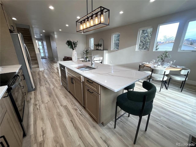 kitchen with sink, stainless steel appliances, a spacious island, decorative light fixtures, and light hardwood / wood-style floors