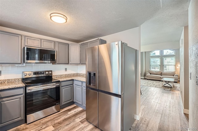 kitchen featuring stainless steel appliances, gray cabinets, tasteful backsplash, and light hardwood / wood-style flooring