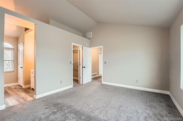 unfurnished bedroom with light carpet, vaulted ceiling, ensuite bath, a spacious closet, and a closet