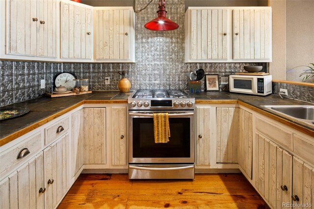 400 W Galena, Moffat, CO 81131 - kitchen with stainless steel gas stove, white microwave, decorative backsplash, light wood-style flooring, and light brown cabinetry