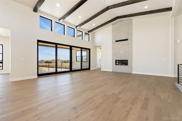 1889 Spring Bloom Dr, Windsor, CO 80550 - unfurnished living room with beamed ceiling, high vaulted ceiling, light wood-style floors, baseboards, and a stone fireplace