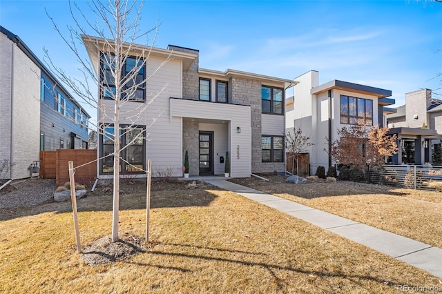 view of front of home featuring stone siding, fence, and a front lawn