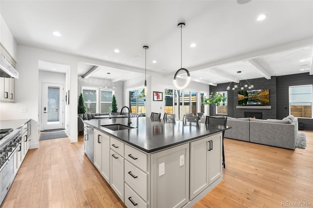 kitchen with light wood-style flooring, a large fireplace, a sink, beam ceiling, and dark countertops