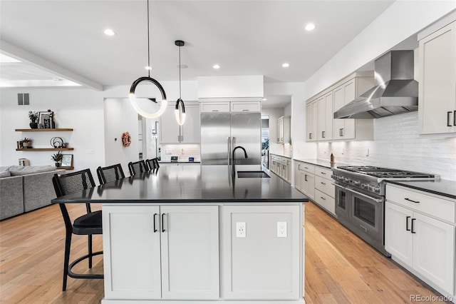 kitchen with a breakfast bar area, a sink, wall chimney range hood, high end appliances, and dark countertops