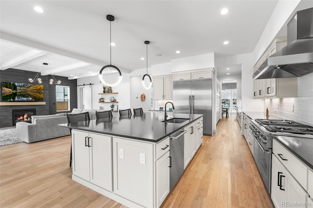 kitchen featuring dark countertops, wall chimney exhaust hood, high end appliances, and a sink