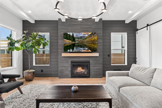 living room featuring a barn door, a fireplace, beam ceiling, and wood finished floors