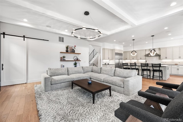 living room with a barn door, beamed ceiling, light wood-style flooring, and visible vents