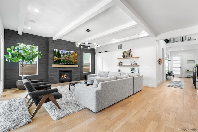 living area with light wood-type flooring, beam ceiling, a fireplace, and a barn door