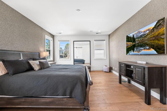 bedroom featuring light wood-type flooring, visible vents, baseboards, and wallpapered walls