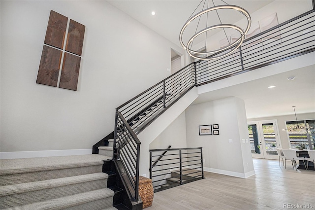 stairs with a towering ceiling, hardwood / wood-style floors, and a chandelier