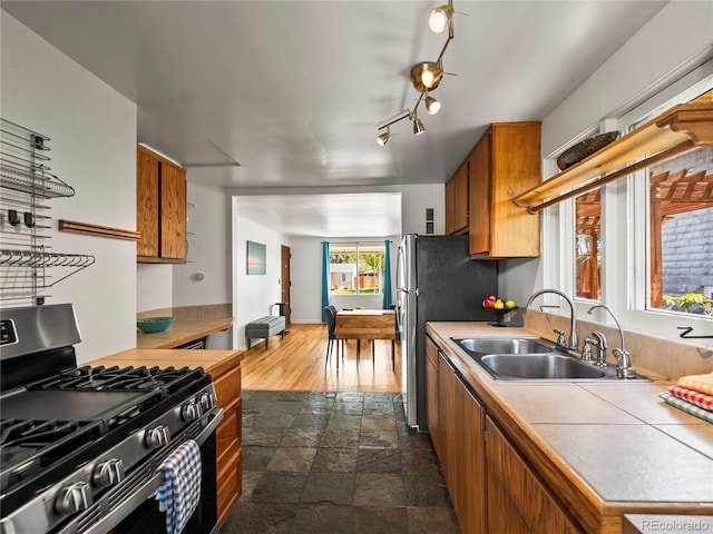 kitchen with appliances with stainless steel finishes, a sink, brown cabinets, dark stone finish flooring, and tile counters