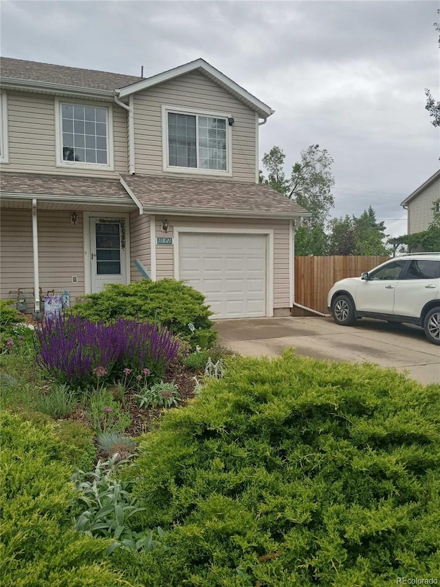 view of front of house with concrete driveway, fence, a garage, and roof with shingles